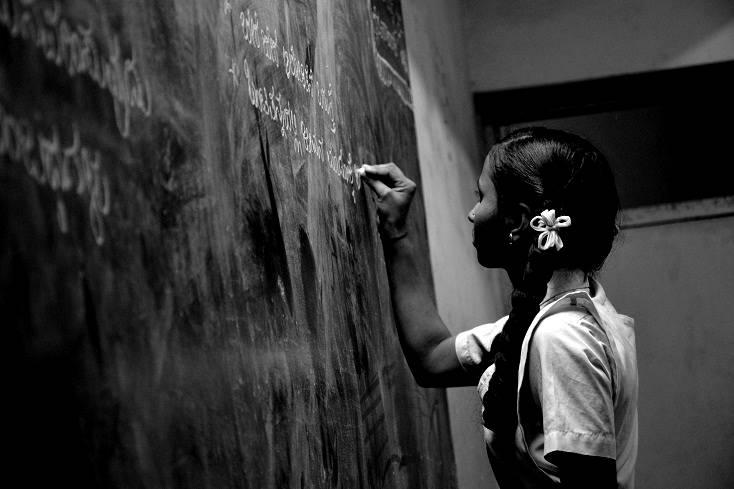 Girl writing with chalk on black board in school